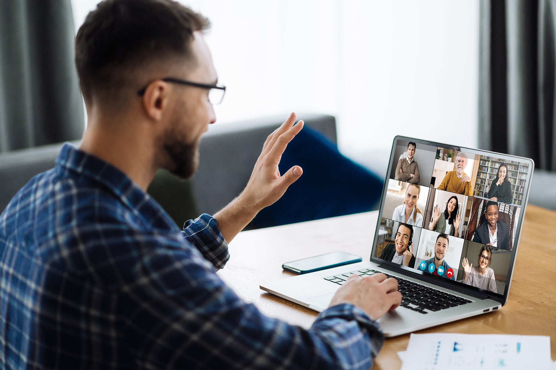 Man in a plaid shirt using a laptop for a video call with multiple people.
