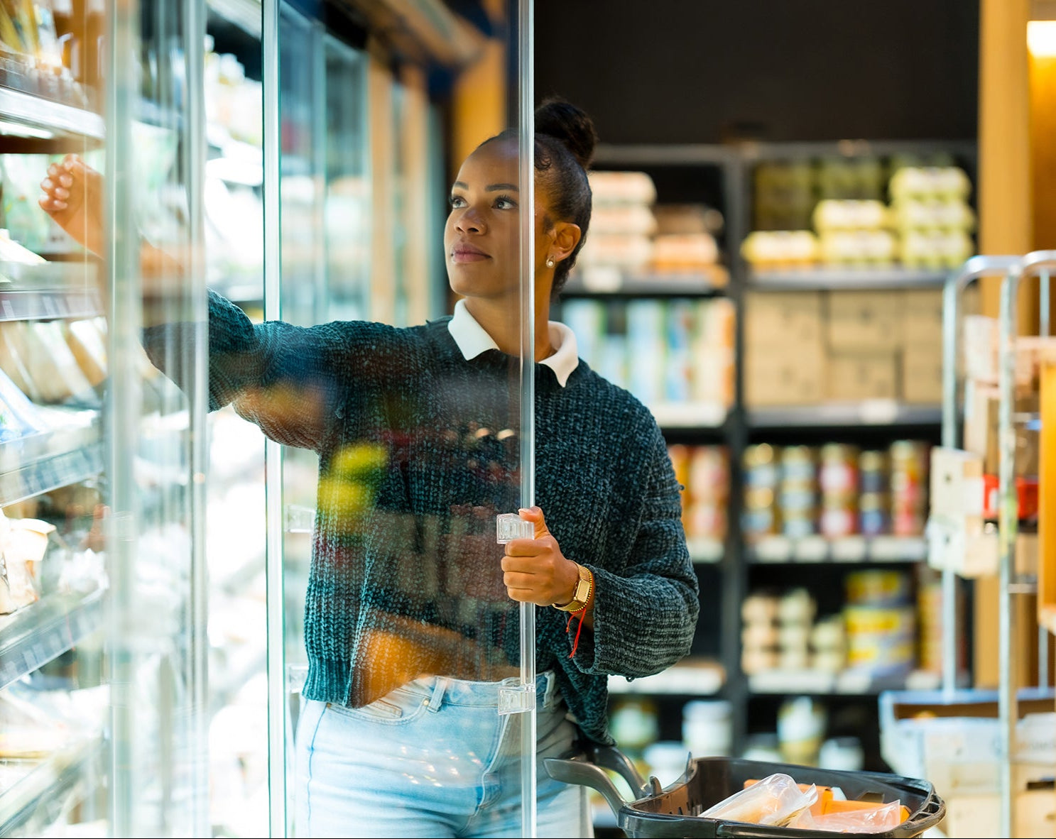 Woman shopping in a grocery store aisle with shelves stocked with products.