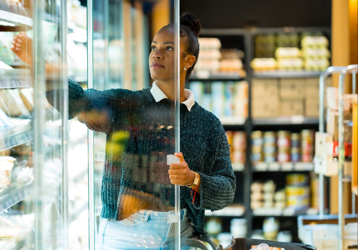 Woman shopping in a grocery store, looking at items on a shelf.
