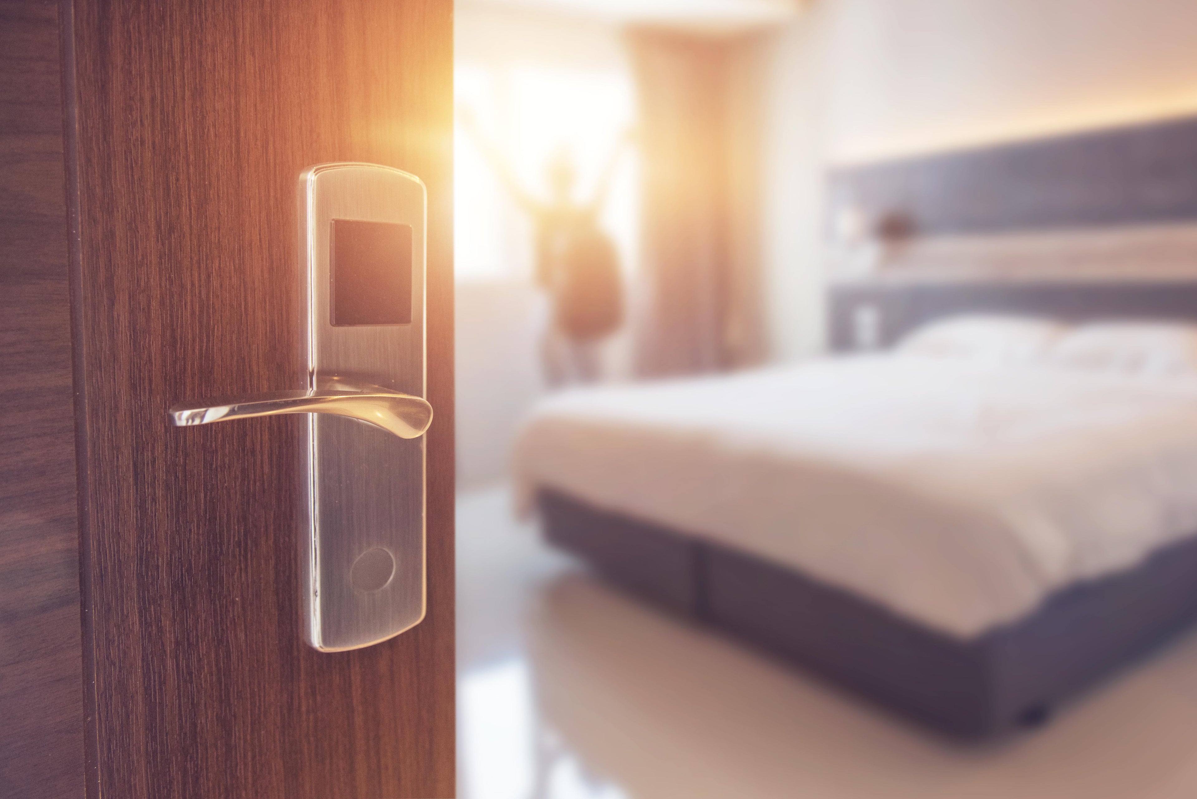 Wooden door with electronic lock handle in a softly lit bedroom within hotel.
