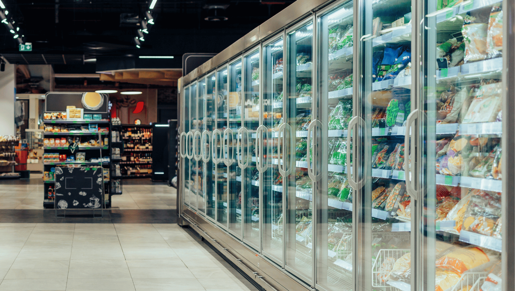 A long row of glass-door refrigerated display cases filled with packaged grocery items in a supermarket aisle.