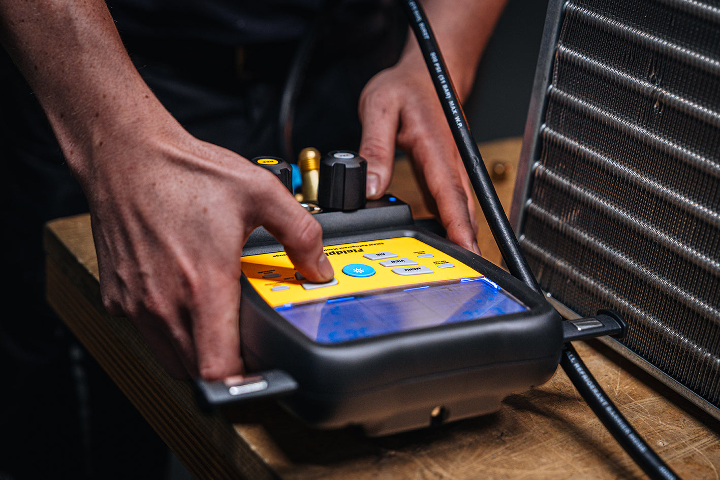 Person interacting with a Fieldpiece digital device on a wooden surface