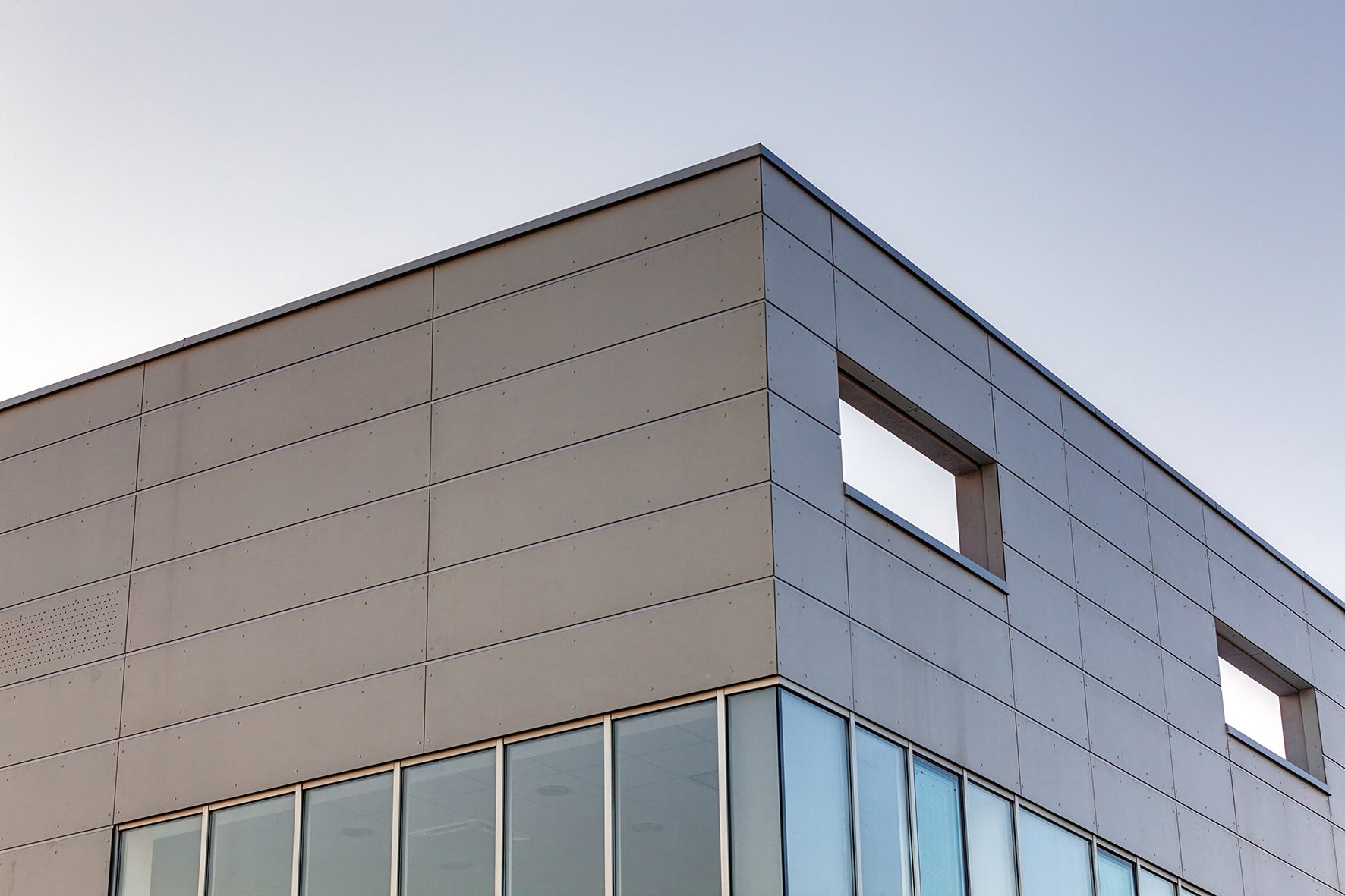 Corner of a modern building with glass windows and a metallic facade.