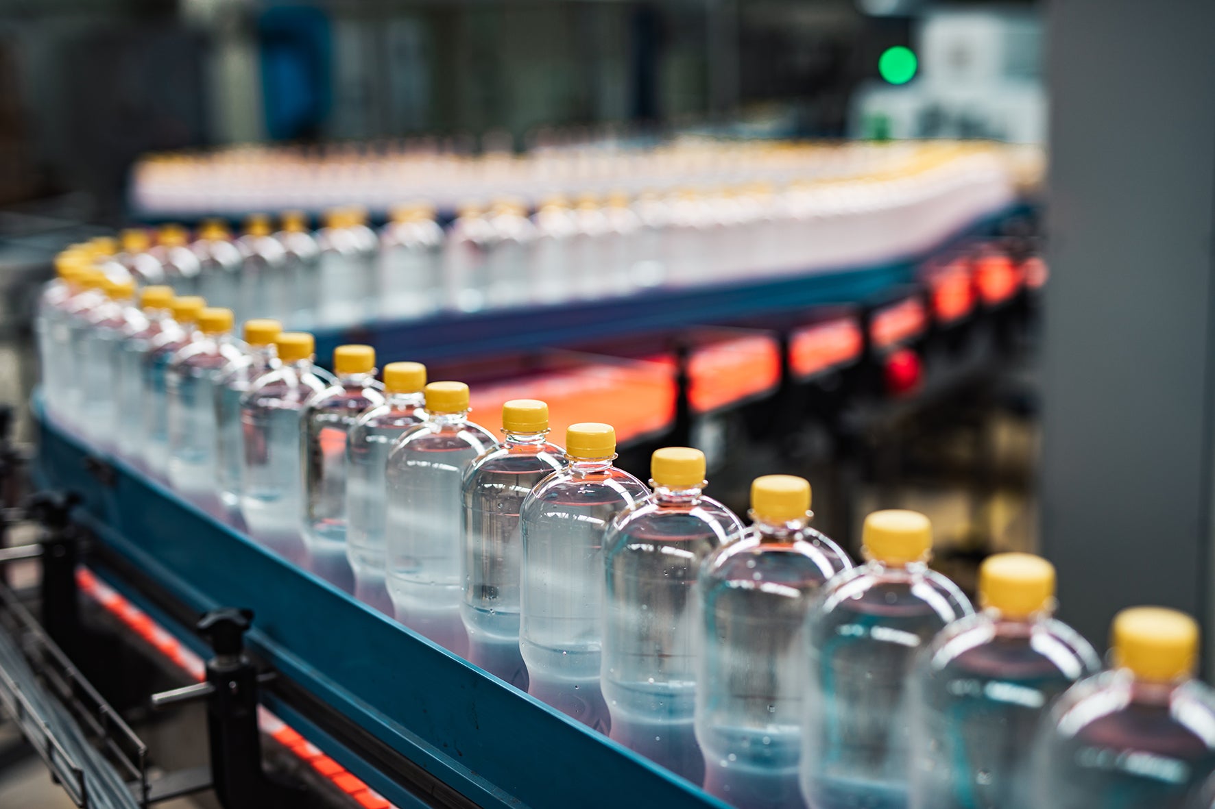 Bottles with yellow caps on a machine in a food processing setting.