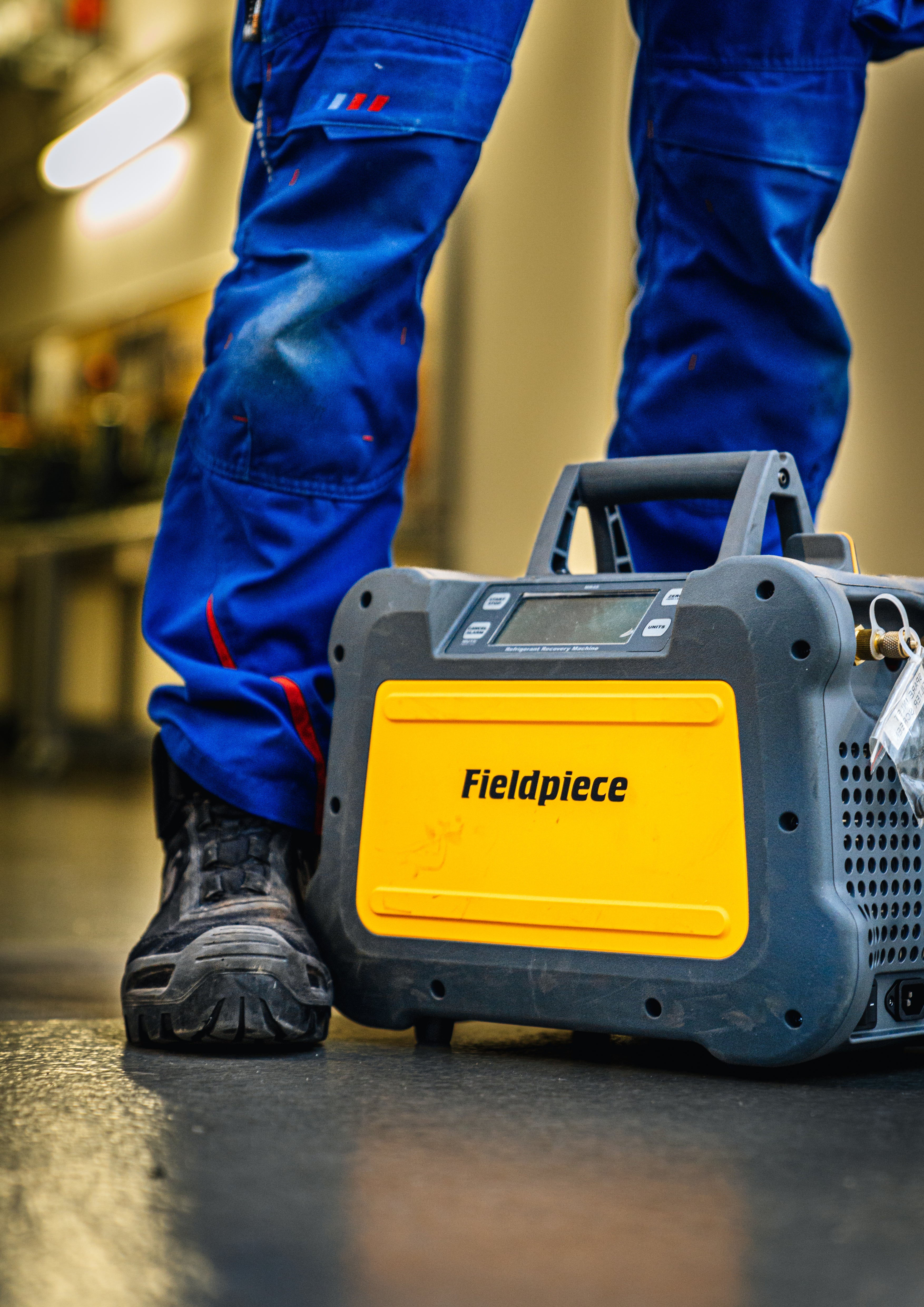 Person wearing blue work pants with a Fieldpiece tool in a workshop setting