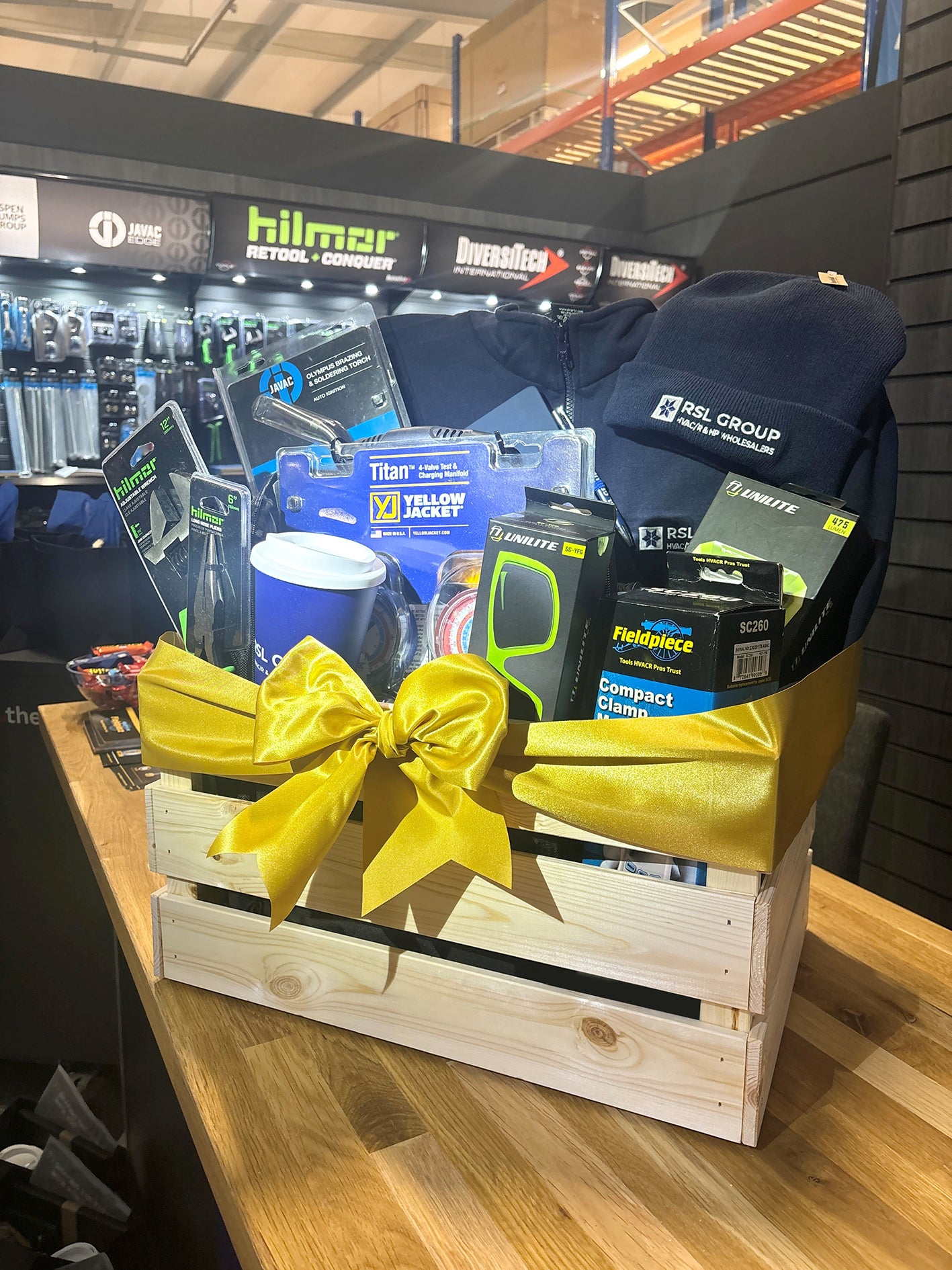 Gift basket with tools and a yellow bow on a wooden surface, with a store interior in the background.