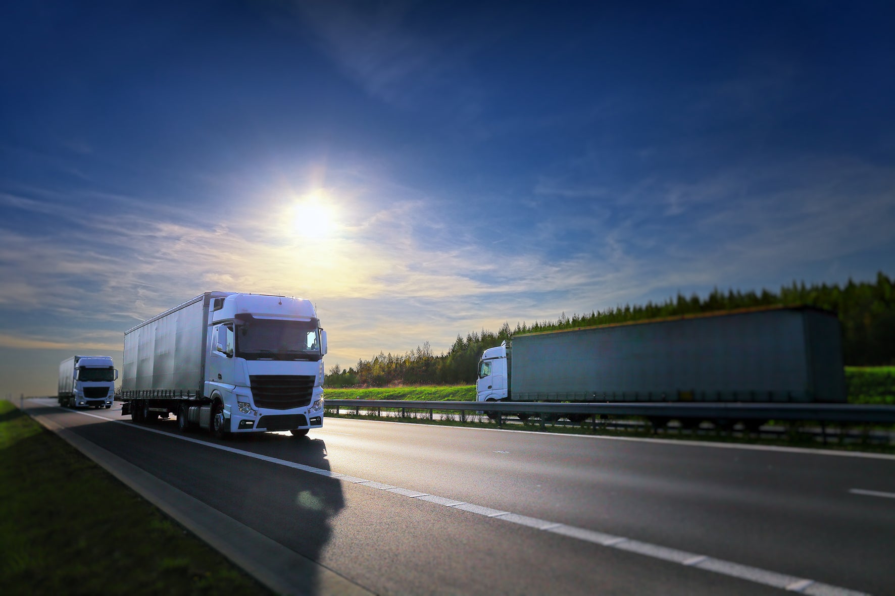 Two trucks on a highway with a clear blue sky and sun in the background.