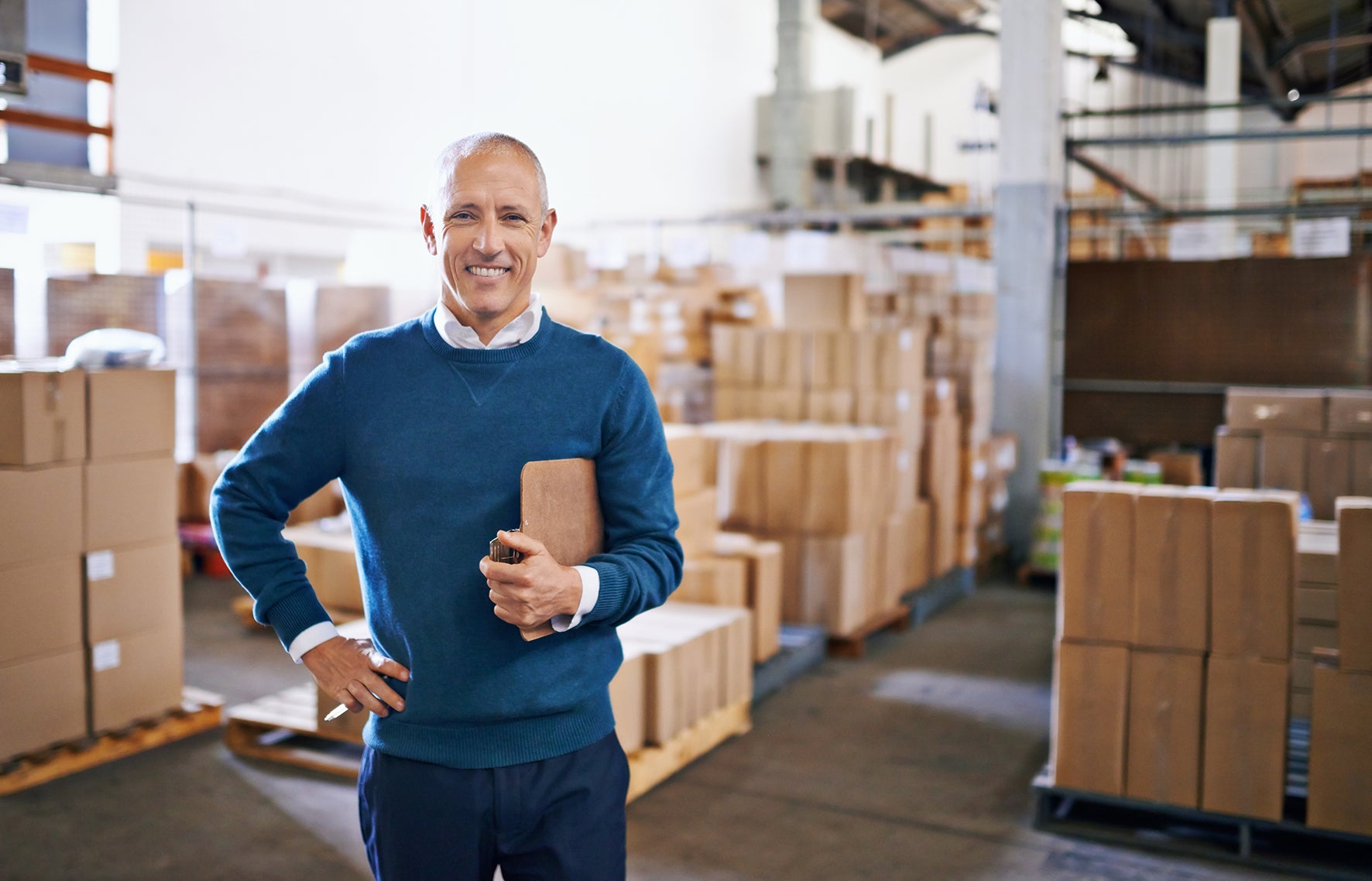Man holding a box in a warehouse filled with cardboard boxes.